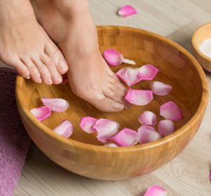 Closeup shot of a woman feet dipped in water with petals in a wooden bowl. Beautiful female feet at spa salon on pedicure procedure. Shallow depth of field with focus on feet.